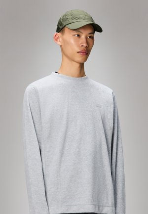 Grå sweatshirt med långa ärmar och rundad halsringning, med en diskret logotyp på bröstet. Tillsammans med en ljusgrön keps.