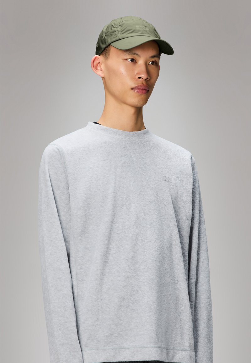 Sweatshirt cinza com mangas longas e decote redondo, apresentando um logo subtil no peito. Combinado com um boné verde claro.