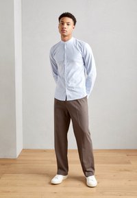 Camicia azzurro chiaro a maniche lunghe con chiusura a bottoni, abbinata a pantaloni marroni e sneakers bianche. Tessuto morbido con un design aderente.