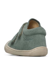 Scarpa slip-on in suede verde tenue con suola in gomma beige, caratterizzata da una forma arrotondata e dettagli cuciti. Fodera interna morbida visibile.