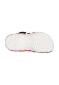 Weiße Gummisohle von Crocs mit einem strukturierten Griffmuster, oberer Teil in Rot und Gelb mit Punkten und einer Schnalle.