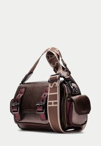 Borsa in pelle marrone testurizzata con accenti magenta, chiusure a doppia fibbia e una tracolla in tessuto staccabile con testo del logo. Forma rettangolare compatta.