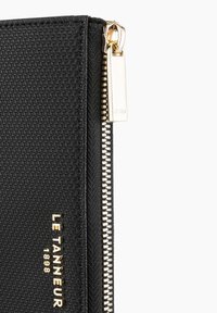Portafoglio nero con zip, realizzato in tessuto texturizzato, con accenti in hardware dorato e logo del brand "LE TANNEUR 1898" in rilievo.