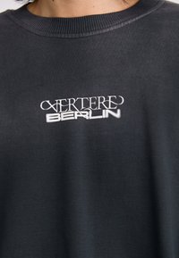 T-shirt in cotone grigio scuro con collo rotondo e testo ricamato bianco centrato che recita "VERTERE BERLIN". Tessuto liscio.