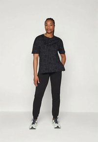 Melna sporta T-kreklu ar īsām piedurknēm, kuram ir ģeometriska raksts, apvienoti ar melnām šaurām biksēm un baltām kedām.