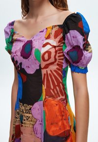 Robe colorée à manches bouffantes avec un mélange de motifs abstraits en violet, vert, rouge et bleu, dotée d'un décolleté carré et d'un tissu léger.