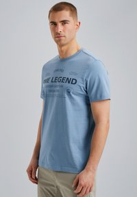 T-shirt en coton bleu clair avec un col rond et des manches courtes ; présente des graphiques en texte imprimé de couleur foncée à l'avant.