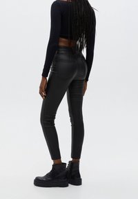 Pantalones de cuero ecológico negros con un diseño ajustado, que cuentan con bolsillos traseros y una textura suave. Combinados con botines negros con cordones.