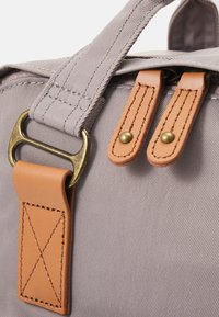 Gray canvas bag with leather accents; features a detachable handle, brass hardware, and stitched details on leather straps.