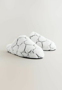 Hvide pelsede hjemmesko med sort syning i et sekskantet mønster, med blød tekstur og lukket hældesign.