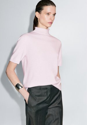 Kortærmet, mock turtleneck sweater i blødt pink stof. Parret med skræddersyede mørkegrå bukser, der har et sølv cuff armbånd som accent.