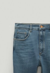 Farkkutakki keskisinisissä, joissa on viiden taskun suunnittelu, napitus ja huomaamaton haalistuminen etupuolella. Tavanomainen vyötärö ja ompelu.