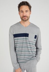 Camisa de manga larga gris con cuello en V, que presenta rayas horizontales en azul marino y verde, y un bolsillo en el lado izquierdo del pecho. Textura suave.