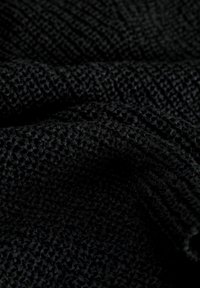 Tejido negro texturizado que presenta un patrón de tejido abierto distintivo, creando una superficie suave y táctil.