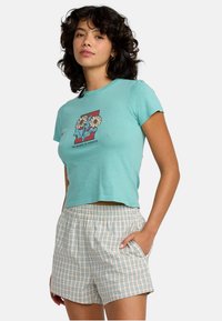 Turkusowy krótki t-shirt z graficznym wzorem kwiatowym; w komplecie beżowe szorty w kratę z elastycznym pasem i bocznymi kieszeniami.