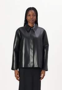 Giacca in pelle nera con finitura lucida, colletto alto, chiusura frontale con bottoni e tasche laterali. Presenta una silhouette ampia e dritta.