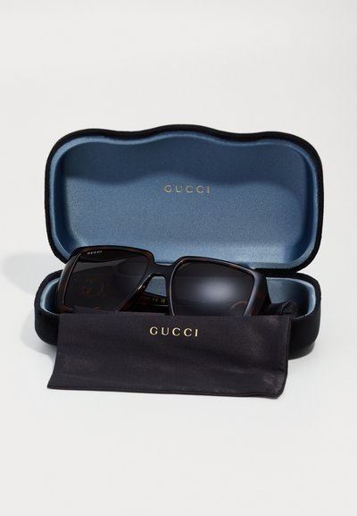 Γυαλιά ηλίου Gucci σε σκληρή θήκη με μπλε εσωτερικό. Οι σκελετοί είναι σε σκούρο χελώνας με φιμέ φακούς. Συμπεριλαμβάνεται και μία μαύρη πετσέτα καθαρισμού.