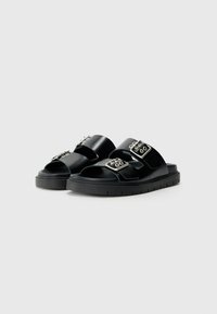 Sandales noires avec une finition en cuir lisse, un design à double bride, des détails en métal argenté et une épaisse semelle noire avec un motif de traction texturé.