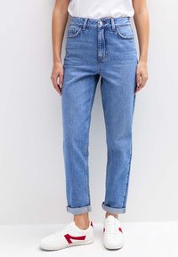 Lichtblauwe jeans met een hoge taille en een losse pasvorm, opgerolde pijpen, voorzakken en contrasterende stiksels, gecombineerd met witte sneakers met rode accenten.