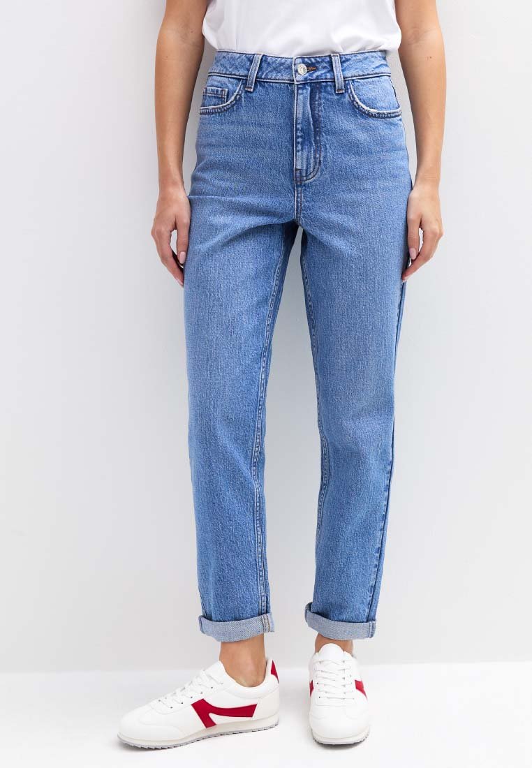 Lichtblauwe jeans met een hoge taille en een losse pasvorm, opgerolde pijpen, voorzakken en contrasterende stiksels, gecombineerd met witte sneakers met rode accenten.