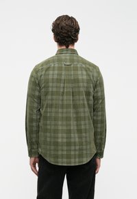 Grønn rutete skjorte med lange ermer, bakyokke og buet hem. Laget av lett stoff med en myk tekstur.