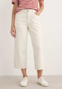 Kreminės plačių kojų kelnes su aukštu liemeniu, su priekinėmis kišenėmis ir mygtuko uždarymu. Derinamos su baltais sportiniais bateliais.