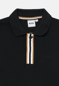 Črna polo majica z dvojnim gumbom in prugastim ovratnikom v beli in bež barvi. Logotip z reliefnim tiskom na levi strani. Piqué tkanina.