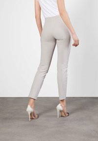 Light beige pants made of smooth material, featuring a slim fit and ankle length. The model wears clear high-heeled shoes.