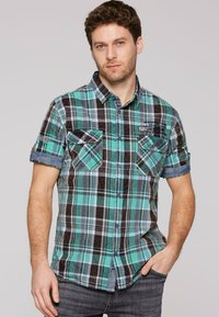 Kratka majica s kratkimi rokavi s karirastim vzorcem v teal, črni in beli barvi. Ima dva žepa na prsih, denim poudarke na rokavih in podrobnosti z logotipom.