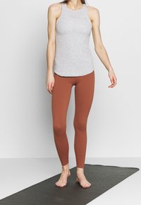 Top grigio senza maniche abbinato a leggings color ruggine. Il top ha una texture liscia, mentre i leggings sono aderenti e elasticizzati.