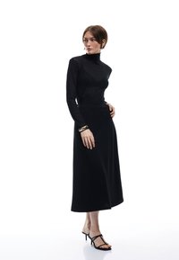 Sort, langærmet turtleneck-top parret med en flydende, gulvlængde sort nederdel. Outfittet har en glat tekstur og en subtil glans.
