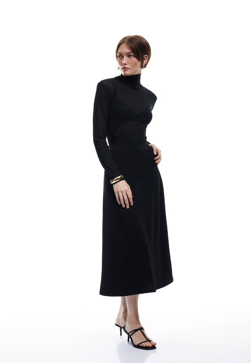 Sort, langærmet turtleneck-top parret med en flydende, gulvlængde sort nederdel. Outfittet har en glat tekstur og en subtil glans.