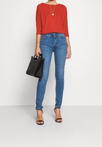 Rød langærmet bluse, blå skinny jeans, sort håndtaske, sorte stiletter. Glat stof med en afslappet pasform, høj talje design.