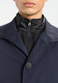 Giacca blu navy con un esterno texturizzato, un colletto interno nero e chiusura con zip. Presenta un singolo bottone e un colletto strutturato.