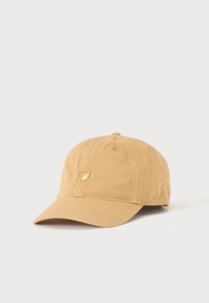 Casquette de baseball brun clair avec visière courbée et petit emblème doré en forme de cœur à l'avant, présentée sur un fond uni clair.