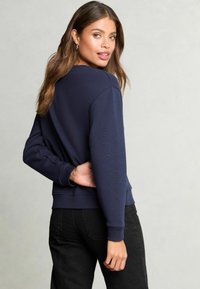 Felpa blu navy con maniche lunghe, polsini a coste e una vestibilità rilassata, abbinata a pantaloni neri. Design semplice, a tinta unita e casual.