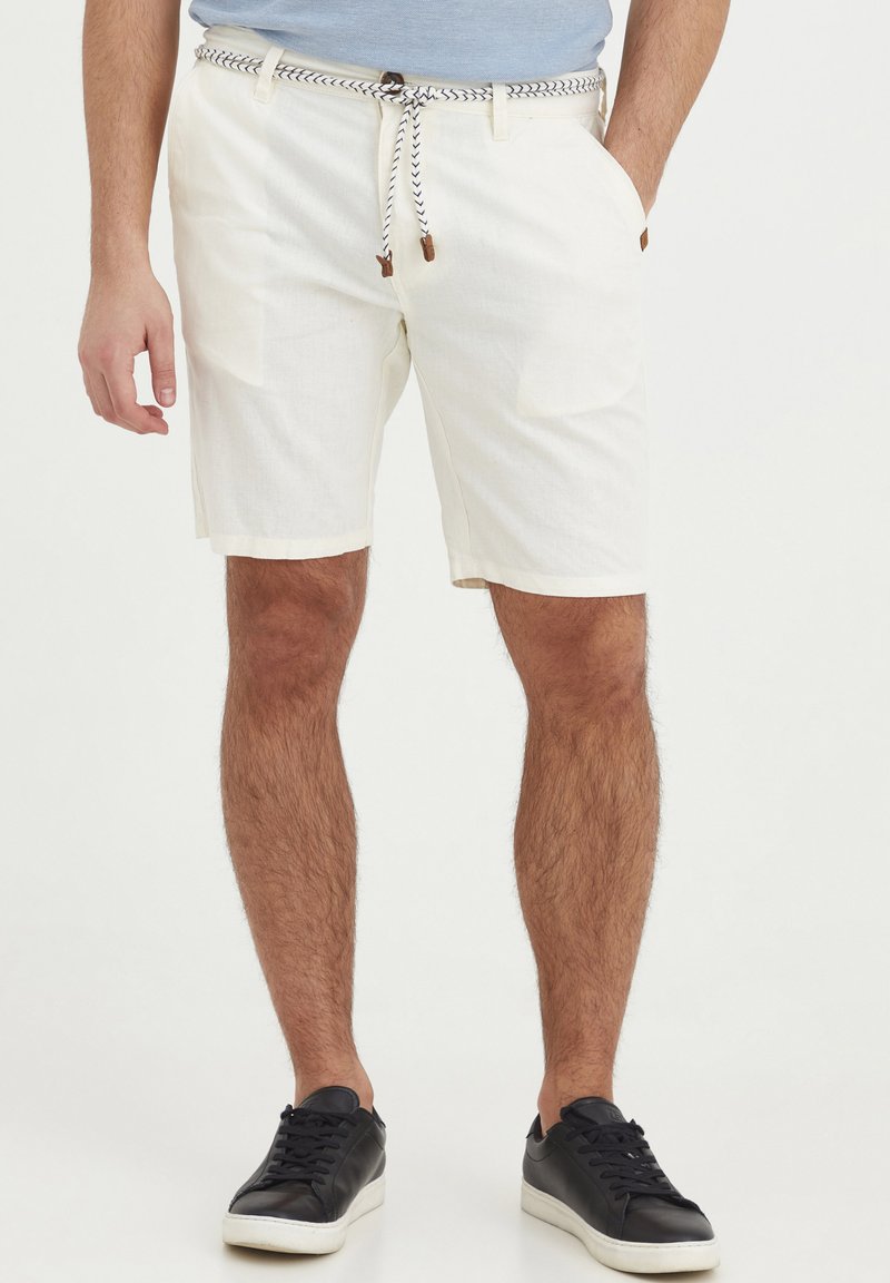 Hvite shorts laget av lett materiale, med to sidelommer, en vevd snøring med brune detaljer, og en avslappet passform.