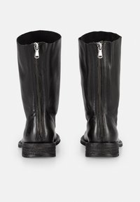 Bottes en cuir noir arrivant au genou avec deux zips à l'arrière, semelles plates et texture lisse. Le design est simple et fonctionnel.