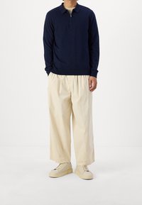 Marinblå stickad tröja med dragkedja vid kragen, beige vida byxor och beige sneakers med tjock sula. Strukturerad tyg, avslappnad passform.