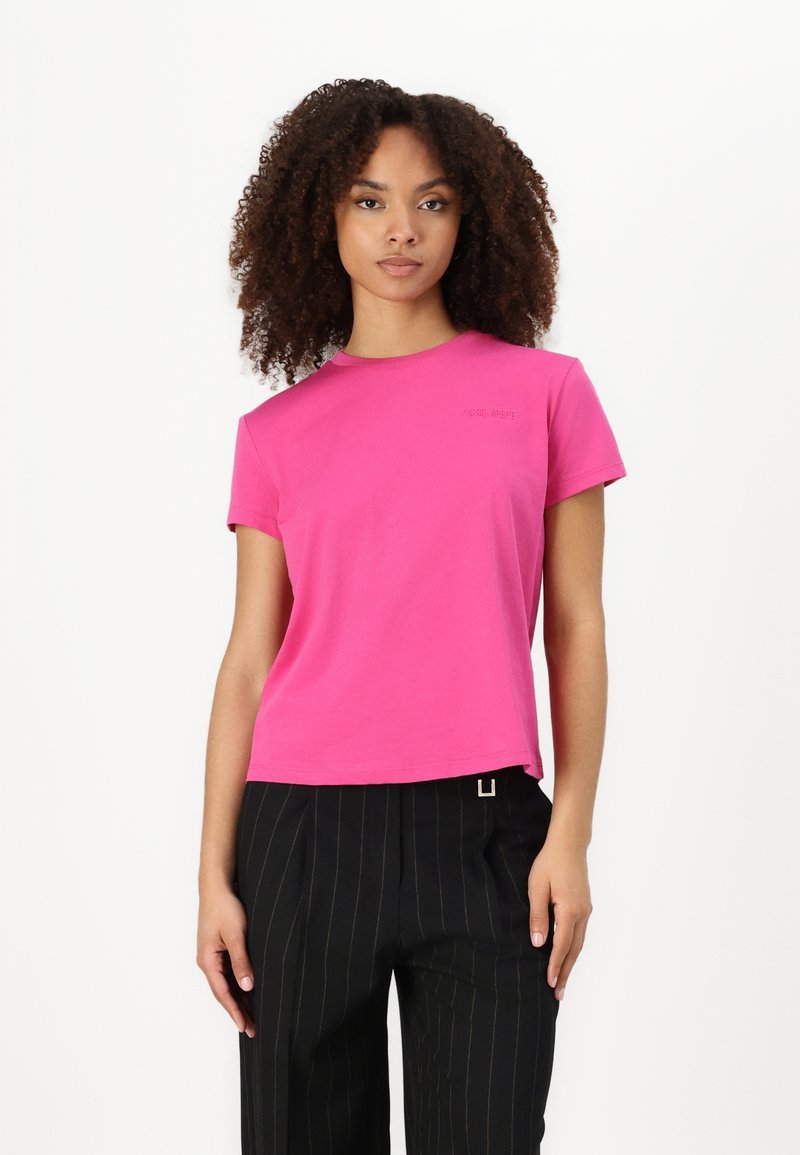 T-shirt a girocollo in cotone rosa con maniche corte, caratterizzato da un sottile logo del marchio sul petto. Indossato con pantaloni neri a righe sottili.
