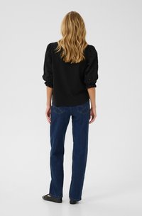 Svart topp med puffärmar av spets, matchad med mörkblå rakbenade jeans. Outfiten har en klassisk design och minimal detaljering.