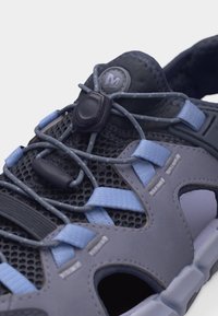 Κοντινό πλάνο ενός γκρι και μπλε αθλητικού σανδάλι με ρυθμιζόμενα ελαστικά κορδόνια bungee και επάνω μέρος από διαπνέον πλέγμα.