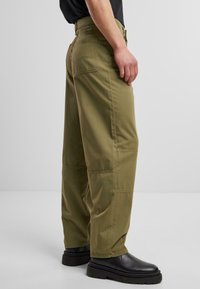 Pantalones cargo verde oliva con un ajuste holgado, que cuentan con bolsillos laterales, un bolsillo trasero y una textura de tejido suave, combinados con botas negras.