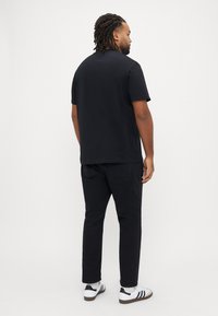 Sort kortærmet t-shirt kombineret med sorte bukser, set bagfra. Hvide sneakers med sorte detaljer fuldender looket.