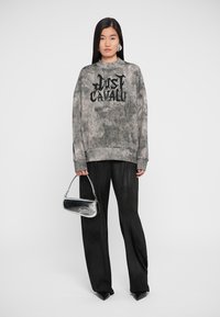 Sweatshirt cinza com gráfico "Just Cavalli" em preto, combinado com calças largas pretas e uma pequena bolsa metálica.