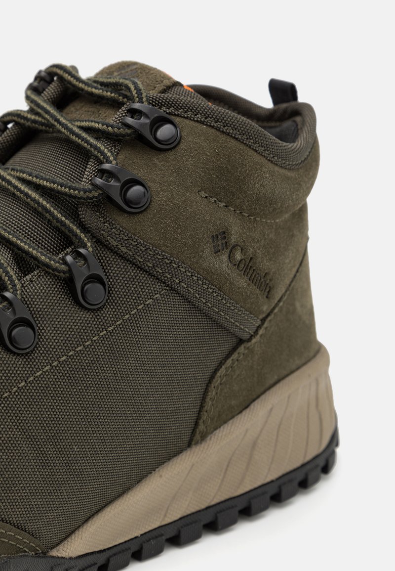 Close-up van een olijfgroene Columbia wandelschoen met zwarte metalen vetersluitingen, een gestructureerde zool en lederen en mesh panelen.