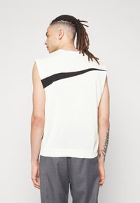Pull crème sans manches avec une rayure noire courbée dans le dos. Tissu en maille confortable, avec un col et un ourlet côtelés.