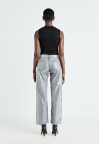 Top negru fără mâneci, asortat cu pantaloni silver cu talie înaltă și croială largă. Pantalonii au cinci buzunare și un ușor luciu, purtați cu tocuri negre.