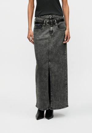 Woman wearing a high-waisted, washed black denim maxi skirt with front slit, black belt, black top, and black pointed-toe boots.