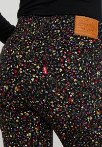 Jeans negros con estampado floral que presentan flores multicolores, un parche trasero de cuero y una pequeña etiqueta roja de Levi's en el bolsillo.